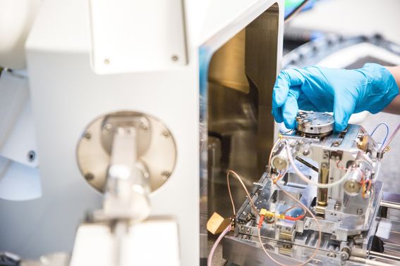 A hand with a blue vinyl glove adjusts complicated research instruments.