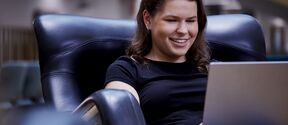 Person sitting on a black leather chair using a laptop.