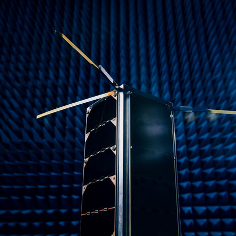 A satellite with extended antennas inside an anechoic chamber with blue pyramid foam panels.
